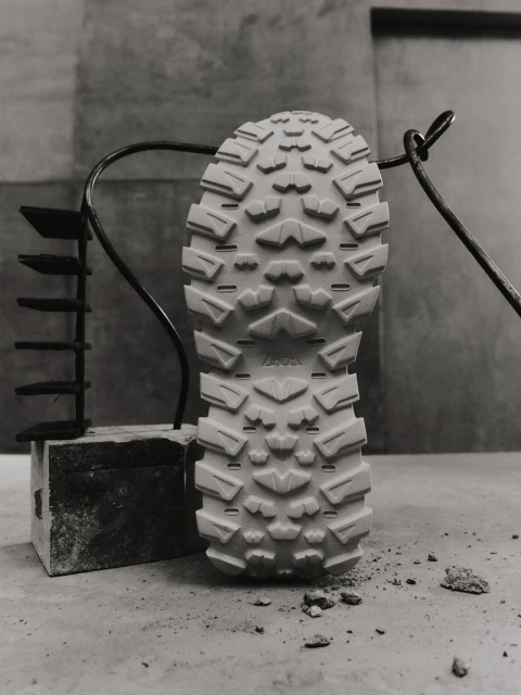 Detailed view of a shoe sole revealing its intricate tread pattern, placed on a stone surface, set against a textured grey backdrop.
