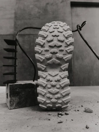 Detailed view of a shoe sole revealing its intricate tread pattern, placed on a stone surface, set against a textured grey backdrop.