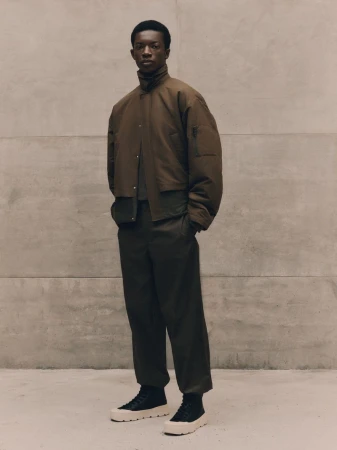 Feranmi Ajetomobi standing in a brown layered jacket and dark trousers against a concrete wall for Zara DUST.
