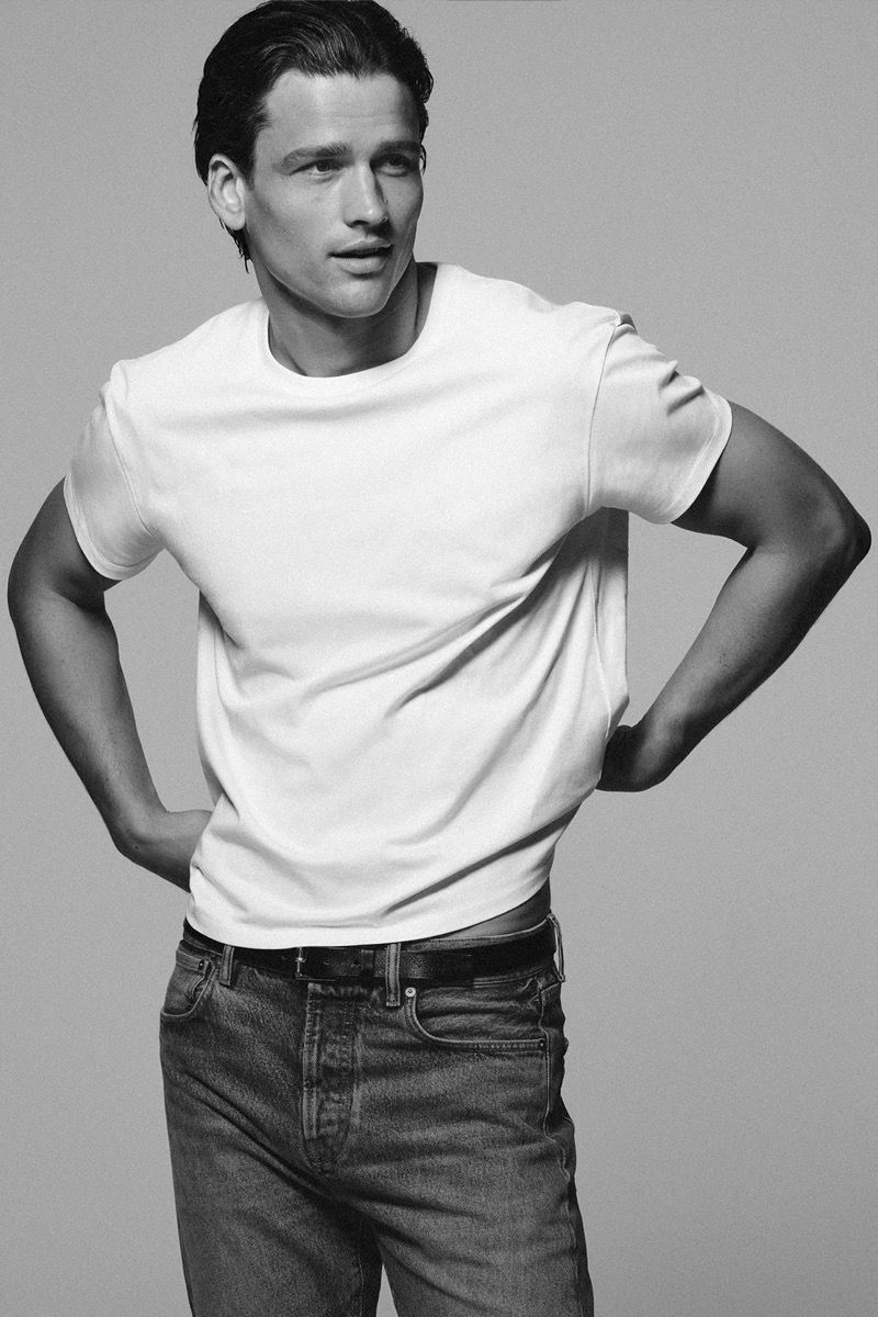 Monochrome portrait of male model wearing a white t-shirt and dark jeans against a grey studio backdrop
