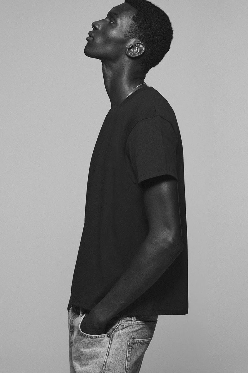 Profile shot of an adult male wearing a black t-shirt and blue jeans, looking upward in a photo studio against a neutral background.