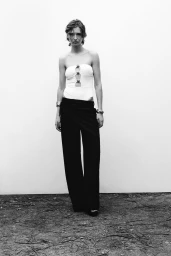 Model wearing a white strapless top with ring details and dark trousers standing against a plain backdrop for Zara project Roe.