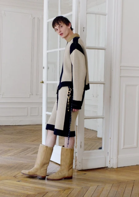 Male model wears an ivory and navy jacket with matching shorts, posing in a minimalist interior near a white door frame. 
