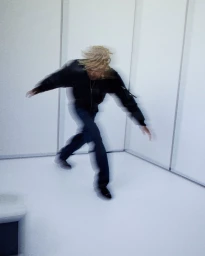 Motion blur photograph of a man wearing a black leather jacket and dark trousers inside a minimalist white room