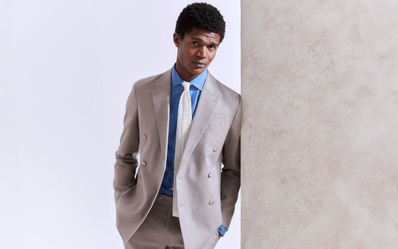 Portrait of a stylish adult male with an afro hairstyle, wearing a suit and tie, standing in an indoor photo studio environment.