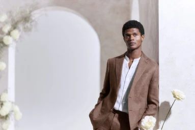 Model O'Shea Robertson wearing a brown suit and white shirt against a neutral arched wall with white flowers.