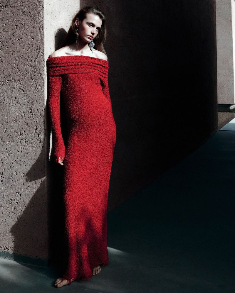 Woman posing in a long red dress against a neutral wall, dramatic shadows and lighting, fashion editorial.