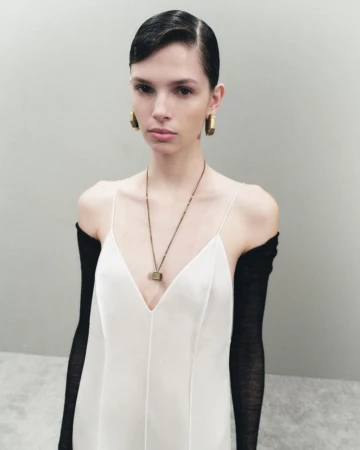 Fashion photo of a female model in a white dress and long black gloves posing in a studio with neutral background. Earring and necklace details.