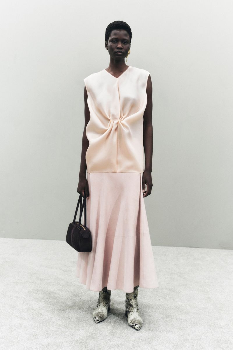 Elegant Black woman poses in a peach-colored sleeveless top and skirt, holding a black purse, with snake print heeled shoes.