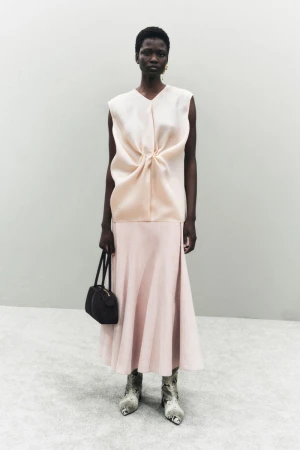 Elegant Black woman poses in a peach-colored sleeveless top and skirt, holding a black purse, with snake print heeled shoes.