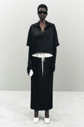 Model in black top and long skirt wearing dark sunglasses against a seamless grey backdrop for Khaite Resort 2025 lookbook