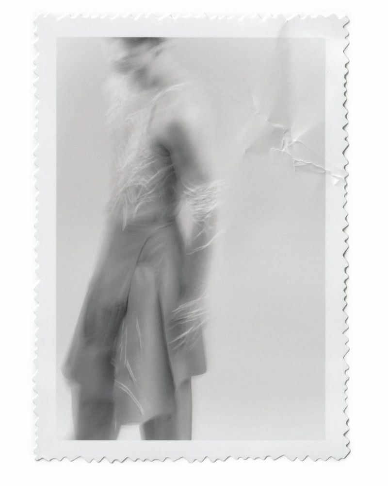 Monochrome photograph of an adult wearing a fringed jacket in a blurred motion, with a decorative white border and textured background.