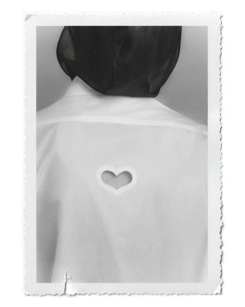 Back view of a person wearing a white shirt with a heart-shaped cutout against a neutral background within a white decorative border.