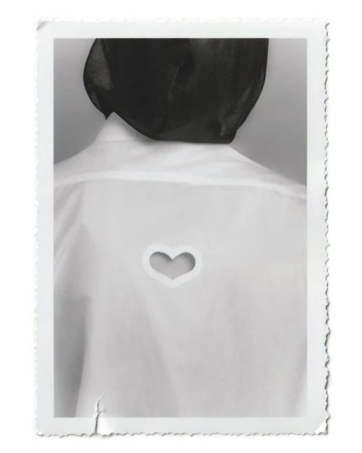 Back view of a person wearing a white shirt with a heart-shaped cutout against a neutral background within a white decorative border.