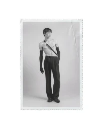 Monochrome portrait of a male model wearing black trousers and long black gloves against a plain studio background.