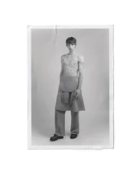 Full-length portrait of a male model wearing a textured top and skirted trousers against a plain studio background.