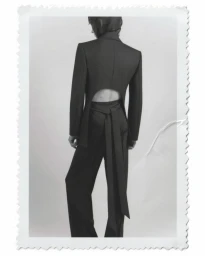 Rear view of a model wearing a tailored black cutout back blazer and matching trousers against a studio background.