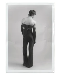Model standing back to camera in dark structured strapless top and trousers against a grey backdrop