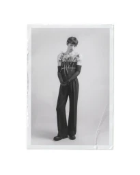 Monochrome fashion portrait of a male model wearing dark trousers and gloves, holding flowers against his chest.