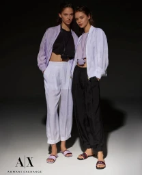 Two female models posing together in casual spring attire against a dark background for Armani Exchange