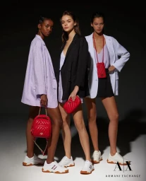 Three female models posing in blazers and white sneakers, each holding a vibrant red handbag for Armani Exchange SS24.