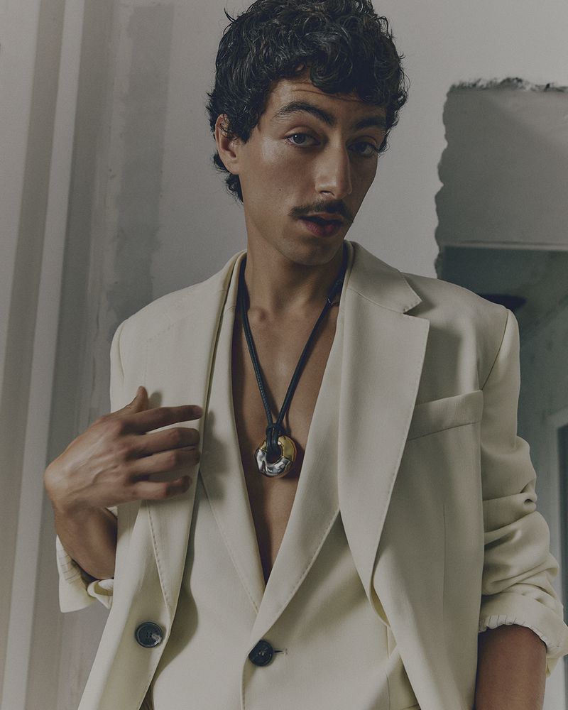 Man in off-white suit with black necklace. Elegant fashion portrait in minimal environment with natural light. Beauty and style concept.