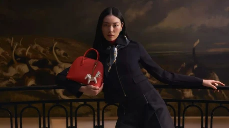 Model Bingbing Liu in a black tailored jacket holding a red leather Hermès handbag against a classical painted mural.