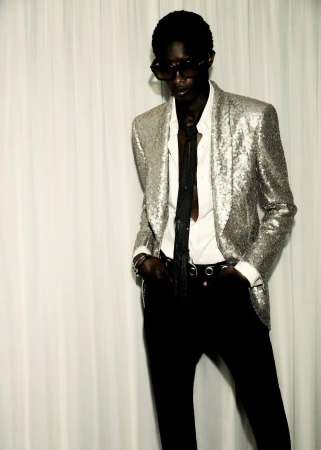 Model in a silver sequin jacket, white shirt, and black pants posing against a neutral backdrop, showcasing high fashion and sophisticated style.