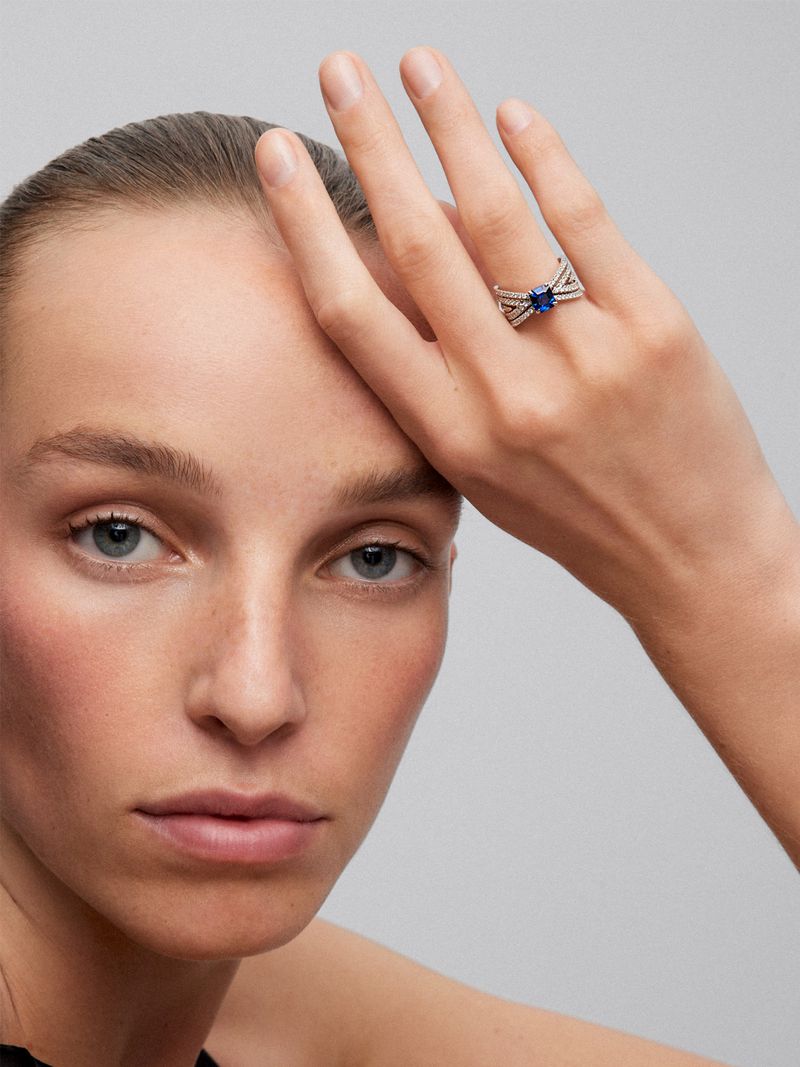 Close-up shot of a woman with fair skin wearing a silver ring with a dark blue stone in a studio setting. Focus on jewelry product shot.