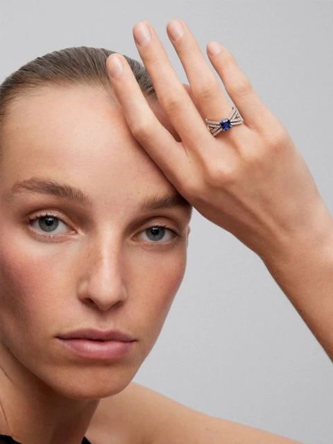 Close-up shot of a woman with fair skin wearing a silver ring with a dark blue stone in a studio setting. Focus on jewelry product shot.