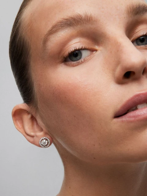 Close-up shot of a fair-skinned adult female with an earring, showcasing jewelry and beauty in a studio setting with neutral background.