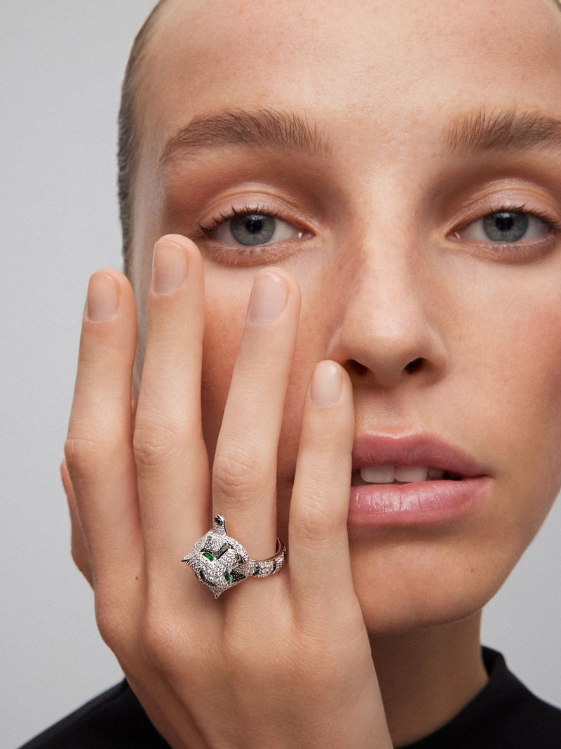 A close-up of a person's face and hand, focusing on the ring with an animal design, showcasing jewelry, beauty, and fashion.
