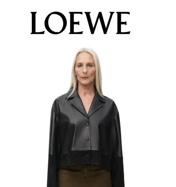 Older adult woman with long gray hair wearing a black leather jacket in front of a white background with the brand Loewe at the top.