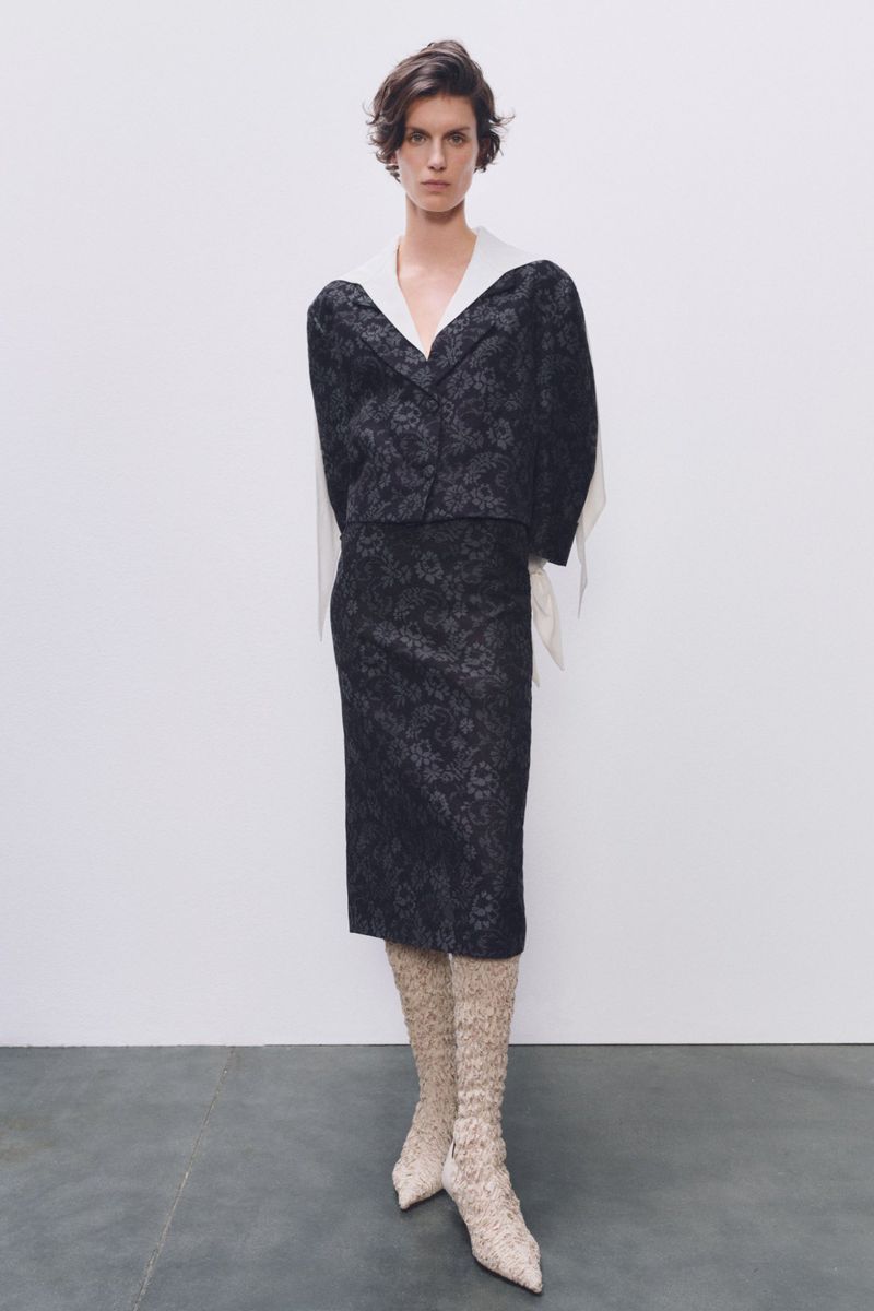 Fashionable woman posing in a studio wearing a floral pattern blazer and skirt with matching floral knee-high boots against a white backdrop.