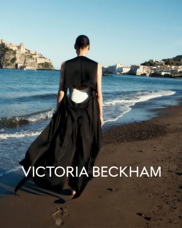 Model Annemary Aderibigbe seen from behind walking along a dark sand beach in a black open-back dress for Victoria Beckham.