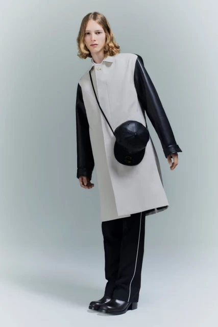 Fashion shot of an androgynous model posing in a studio wearing an off-white color-blocked trench coat with a black cap bag.