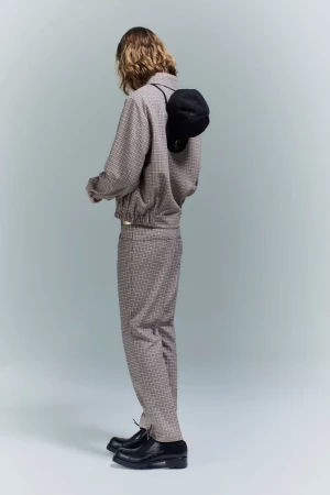 Model seen from behind wearing a patterned grey jacket and matching trousers with a black cap on the back in a studio setting.