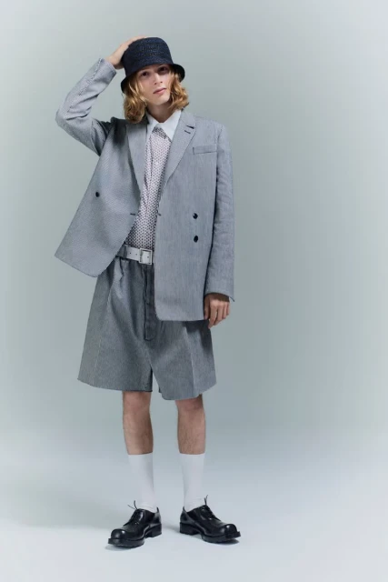 Full-length studio shot of a young adult male model wearing a striped suit, bucket hat, and white socks, posing against a plain background.