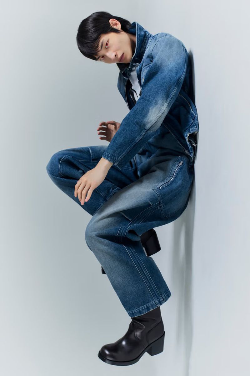 Model Woojin Ham poses in a blue denim jacket and matching jeans with black heeled boots against a white studio wall.
