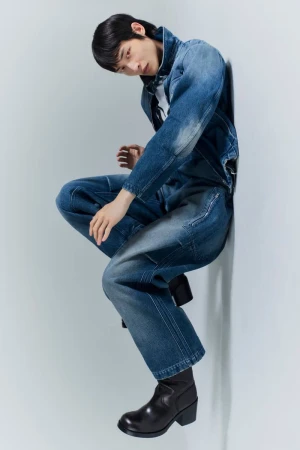 Model Woojin Ham poses in a blue denim jacket and matching jeans with black heeled boots against a white studio wall.