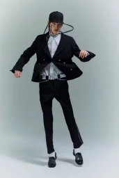 Model in black suit and baseball cap posing against a neutral grey studio background for Random Identities