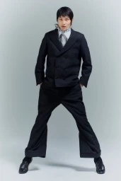 Woojin Ham wearing a black double-breasted suit with flared trousers and a silver chain necklace against a grey backdrop.