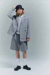 Model wearing a grey double-breasted blazer, matching shorts, and a dark bucket hat against a neutral backdrop