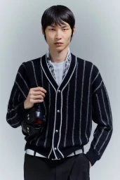 East Asian male model wearing a black vertical-striped knit cardigan over a white top against a grey studio background.