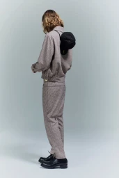 Model seen from behind wearing a patterned grey jacket and matching trousers with a black cap on the back in a studio setting.