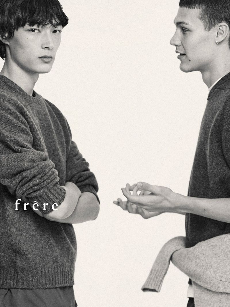 Two adult male models wearing sweaters in a studio setting, showcasing minimalist fashion and neutral tones.