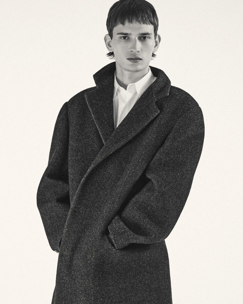 Male model wearing a dark wool coat and white shirt against a plain white background
