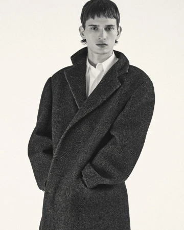 Male model wearing a dark wool coat and white shirt against a plain white background