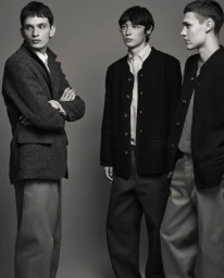 Three male models posing in tailored jackets against a solid grey background for Frere