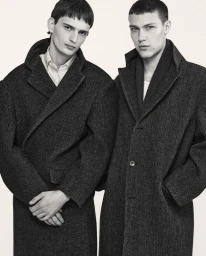Two male models wearing dark tweed coats standing against a neutral background for Frere